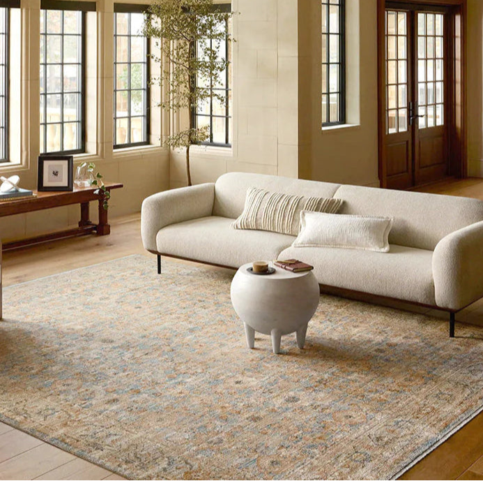 Modern living room with a beige sofa, wooden coffee table, and large windows.